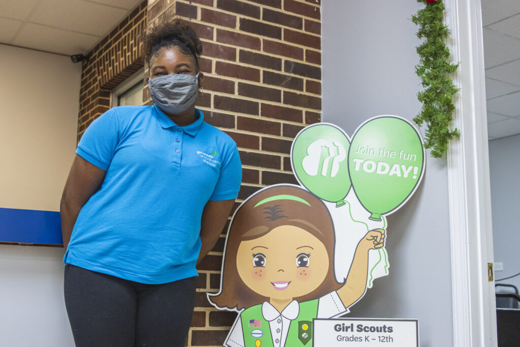 A black woman stands next to a cardboard cutout of a girl scout