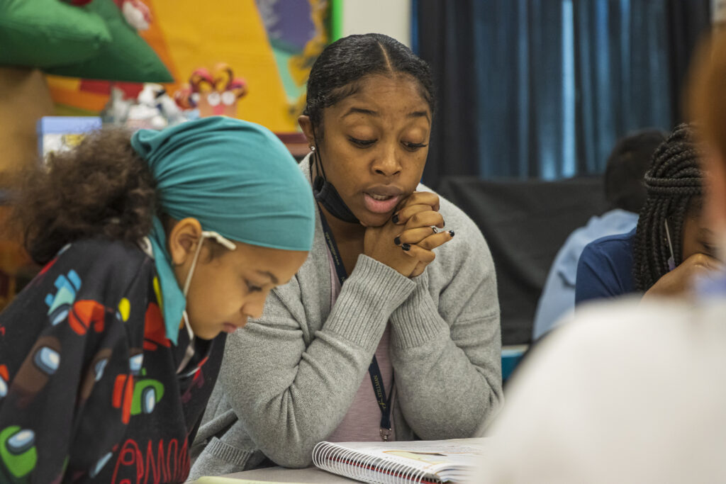 A black female teacher helps a young elementary student read