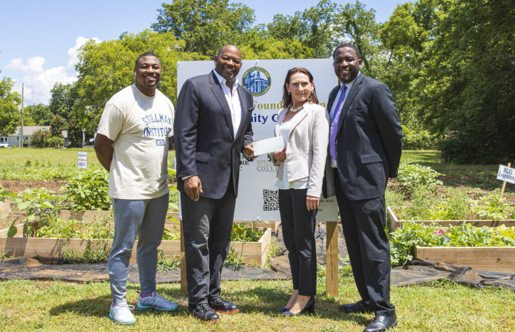 Three black men and a white woman pose in front of a community garden