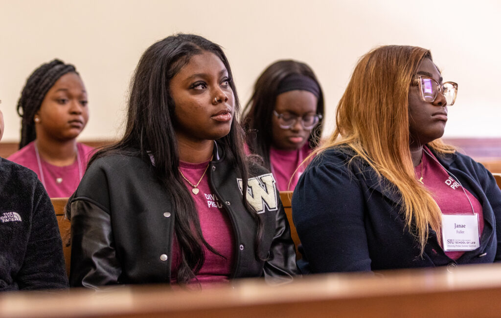 Four black women sit in a courtroom and listen to a presenter