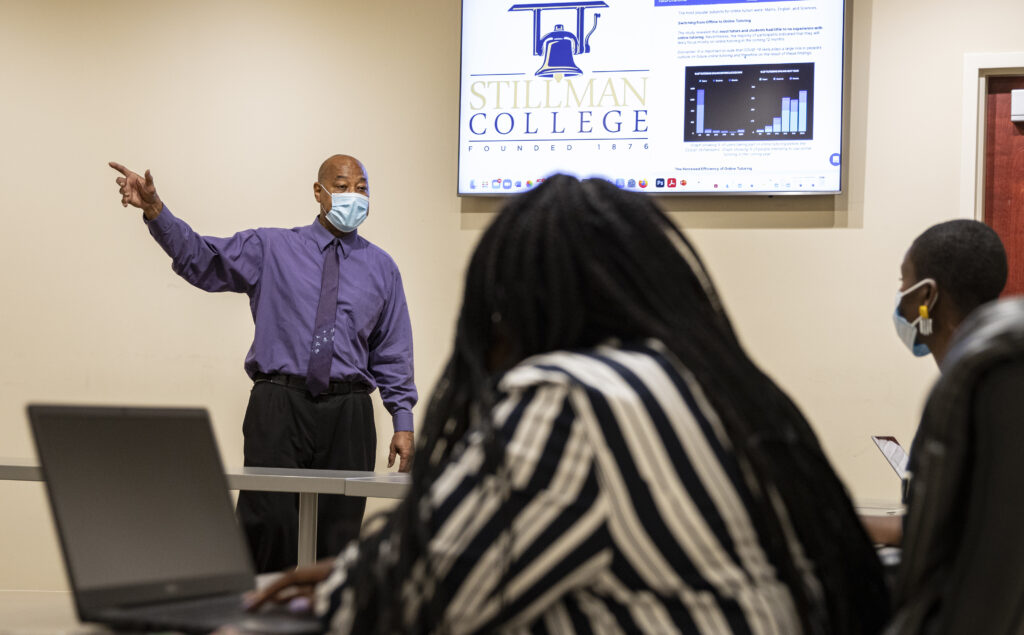A black man talks while giving a digital presentation in a classroom