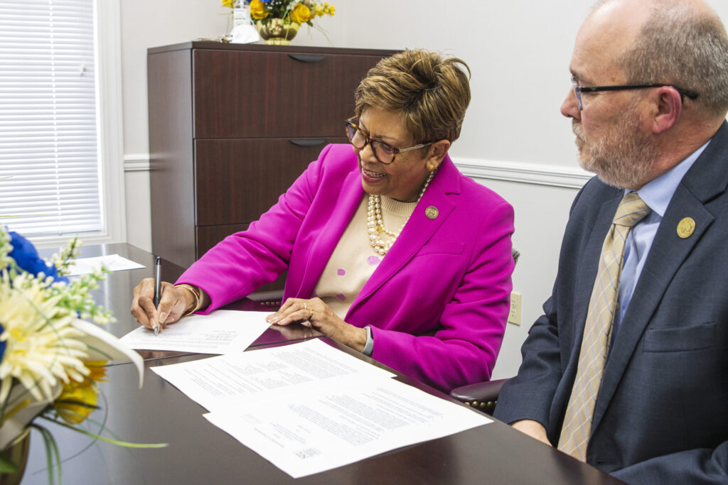 A black woman and white man sign papers at a table