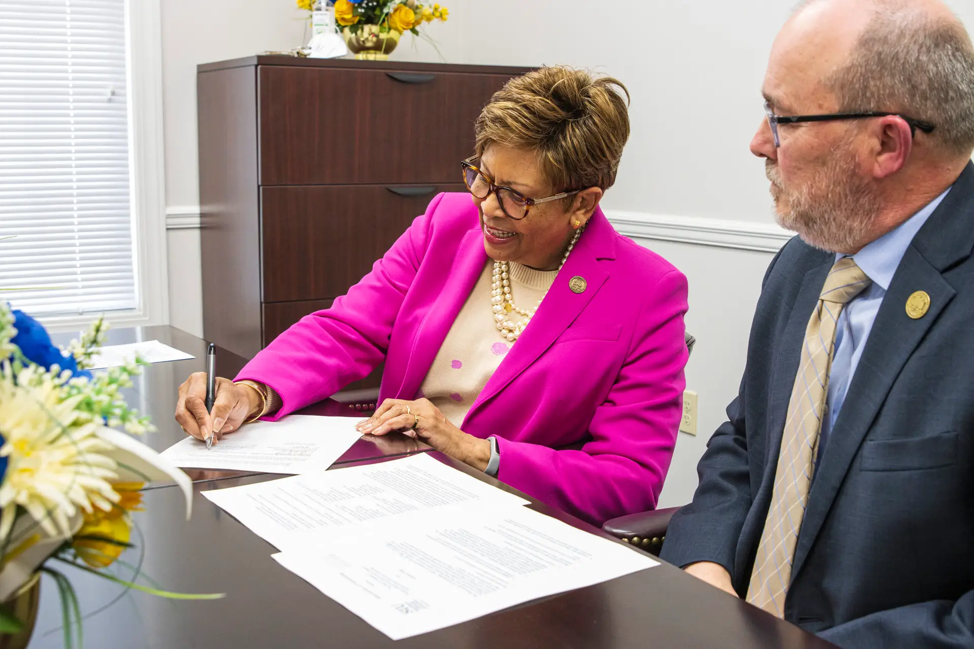 A black woman and white man sign papers at a table