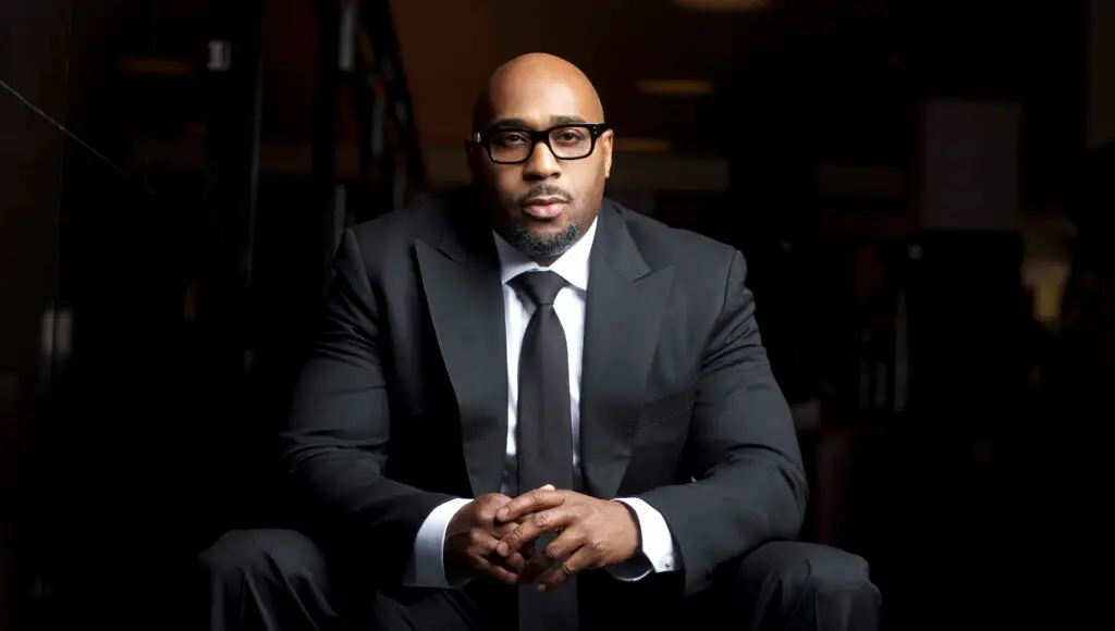 A black man poses for a photo in a dimly lit room