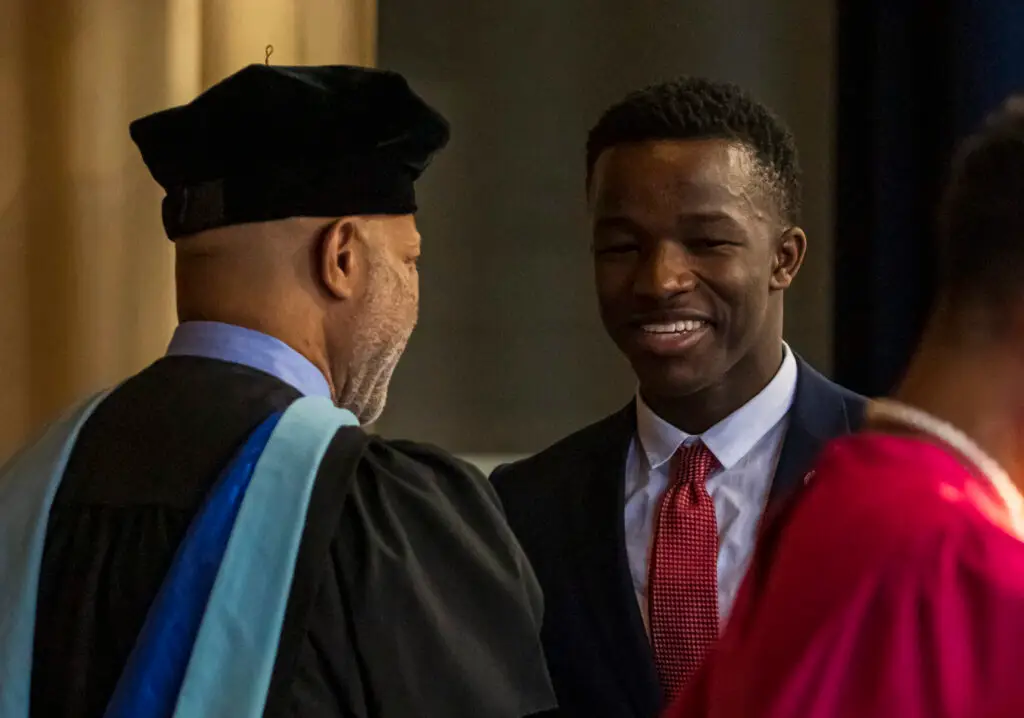 A black male college student shakes hands with a professor
