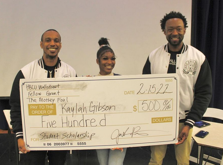 A black female college student and two black men hold an oversized check