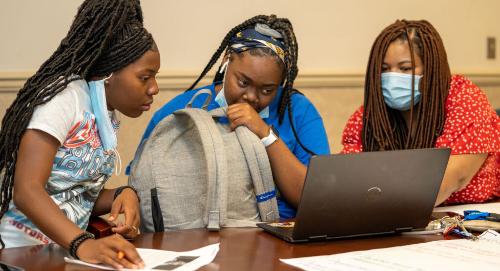 Three Black women site at a laptop computer