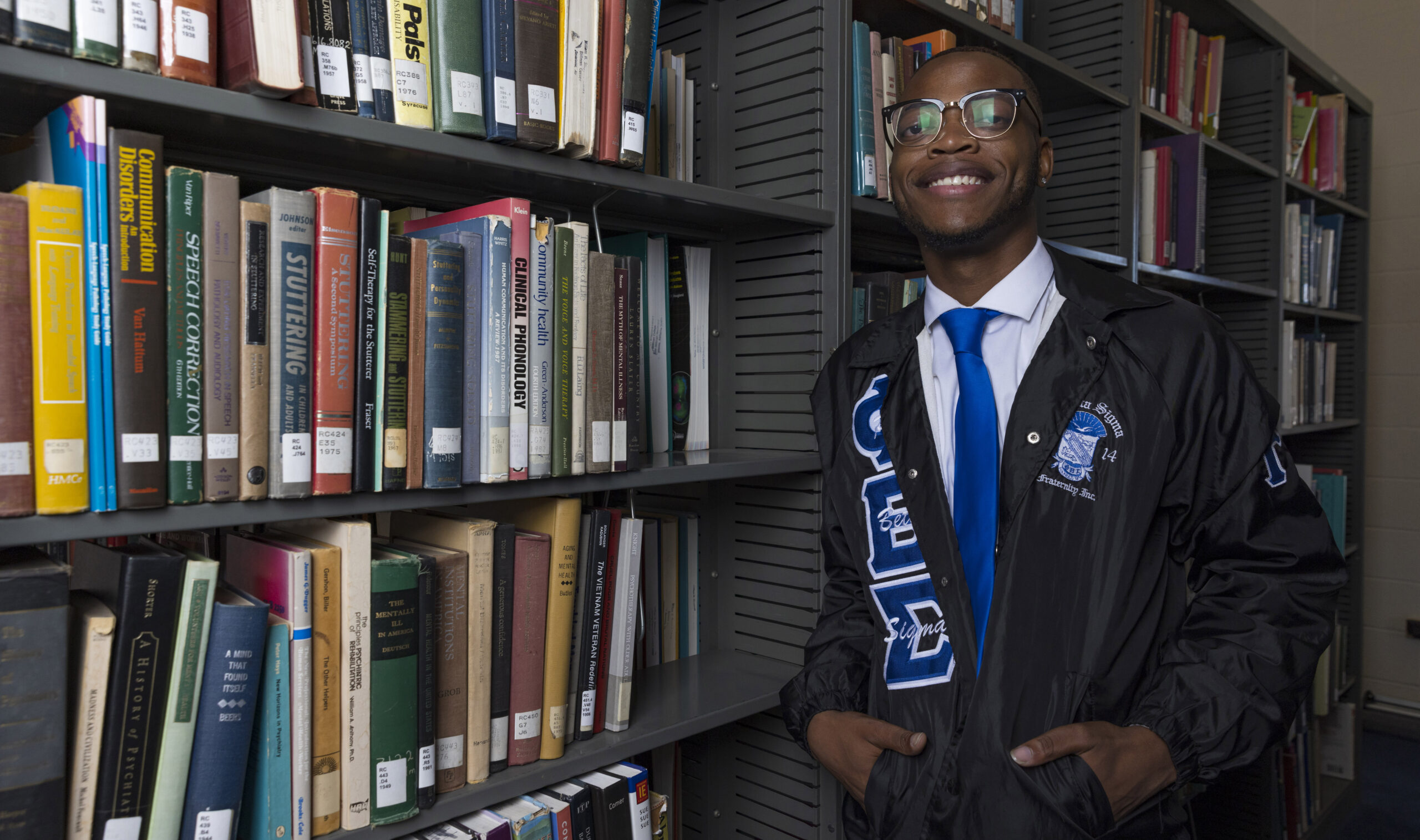 A young black man poses for a photo in a library