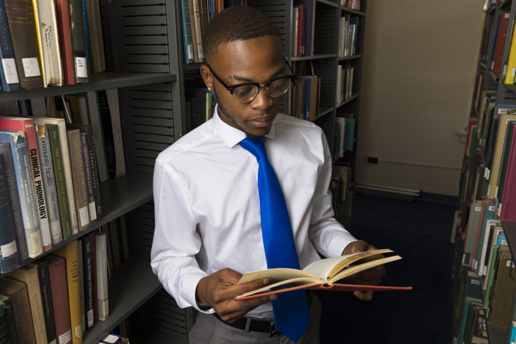 A young black man reads a book in a library