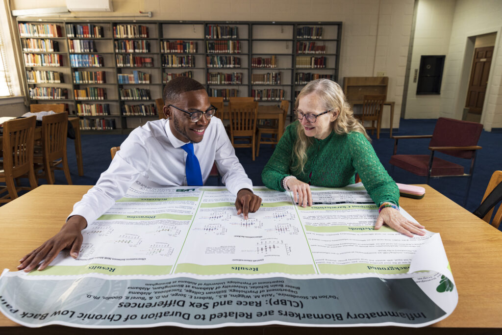 A young Black man and older white woman review a research poster in a library