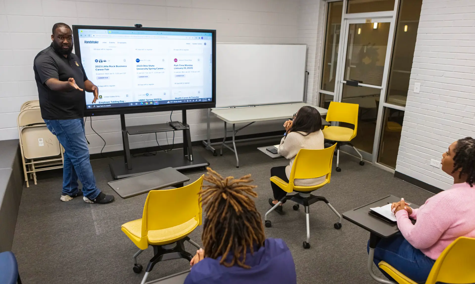 A black college instructor stands at an interactive board while teaching three black students