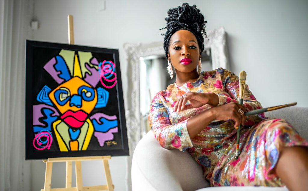 A Black female artist poses next to artwork