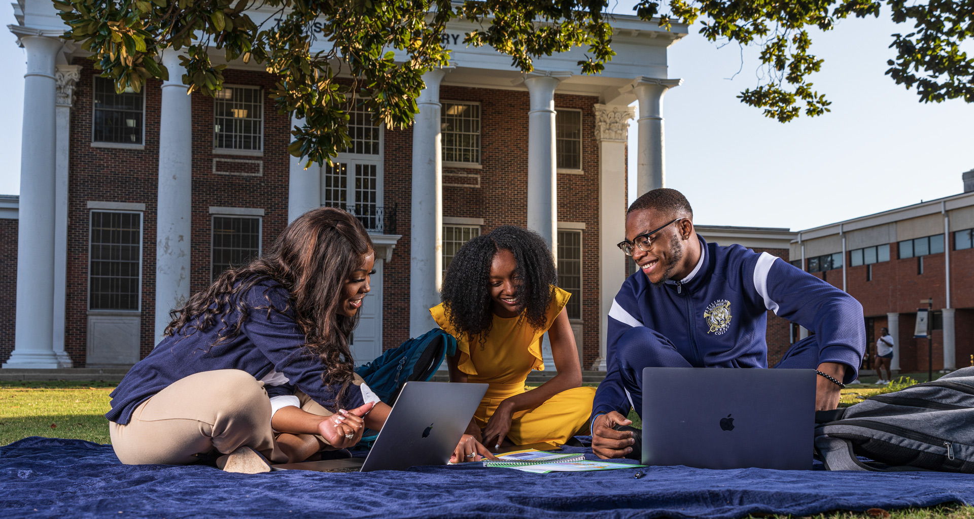 One African American male students studies with two black women under a magnolia tree