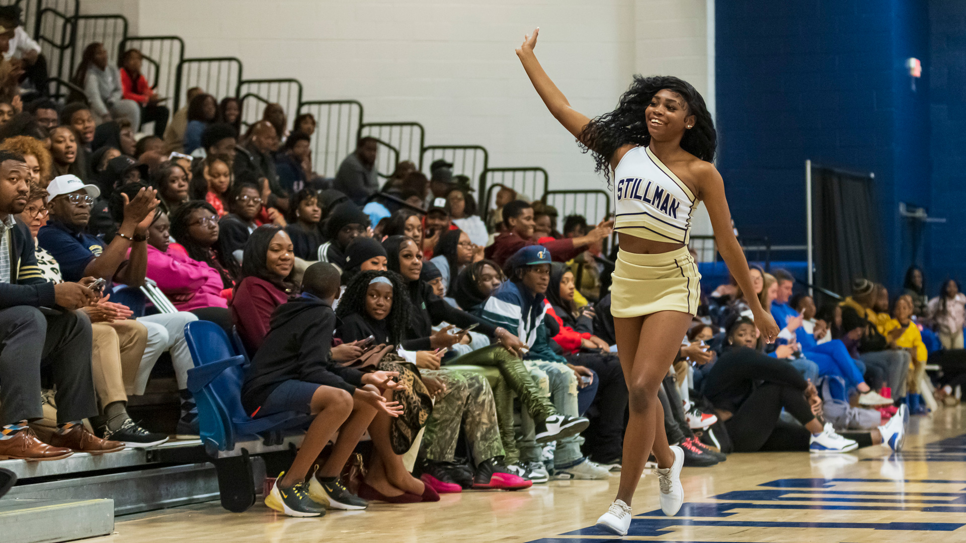 A black female college cheerleader waves to a crowd at a basketball game