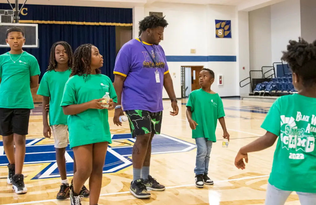 A black male college student walks with young black youth on a basketball court