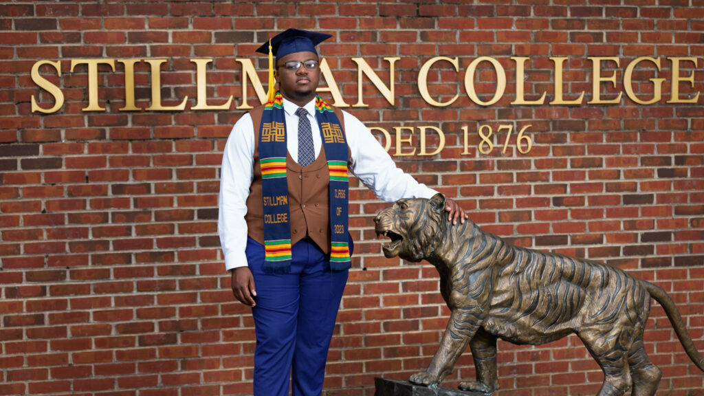 A black male college student poses for a photo next to a lion statue