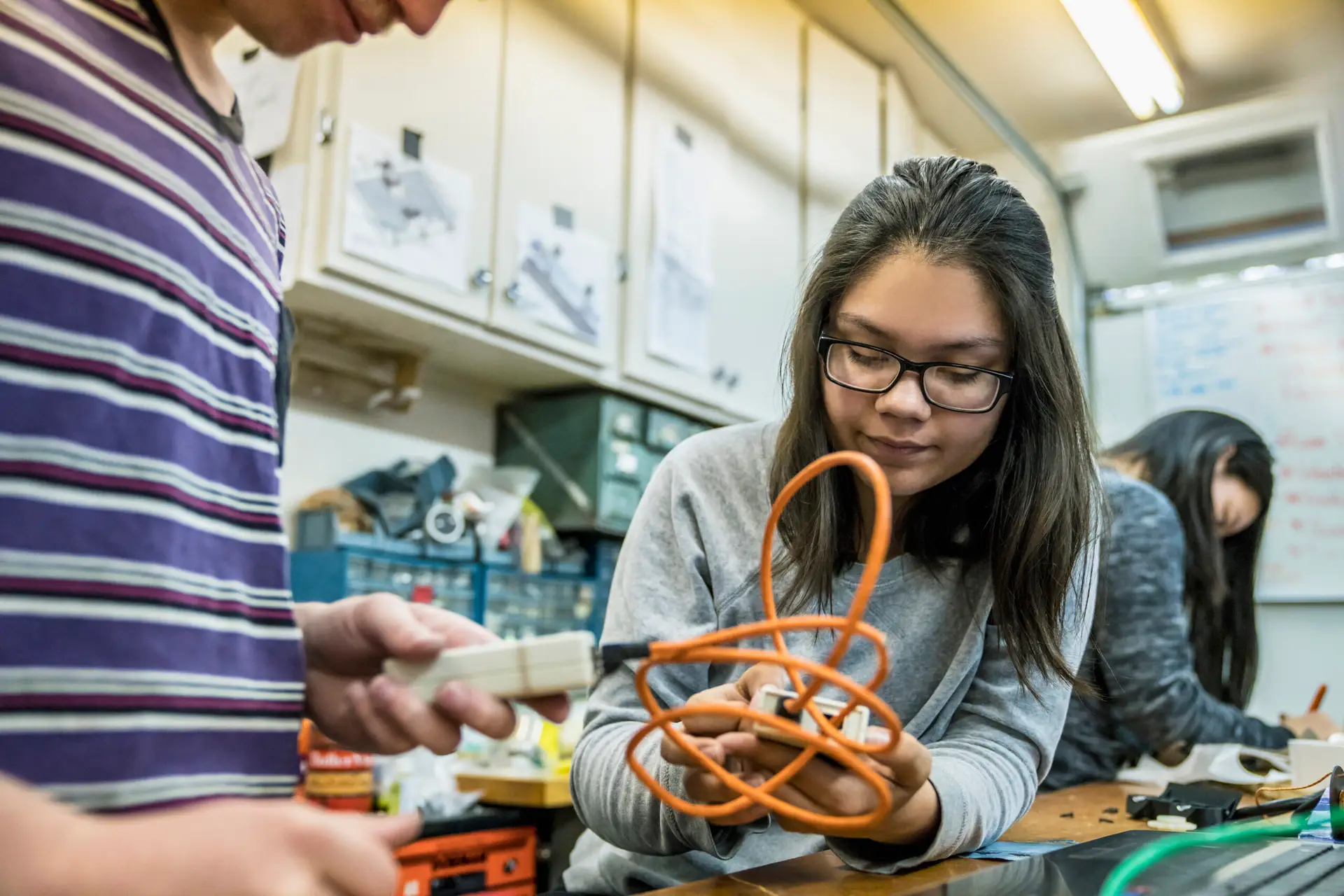 A hispanic female middle school student connects wiring on a robot during a school project